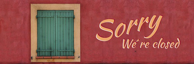 Ein Fenster mit geschlossenen, grünen Fensterläden in einer rotbrauenen Wand. Daneben steht "Sorry We´re closed"