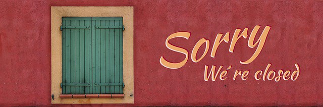 Ein Fenster mit geschlossenen, grünen Fensterläden in einer rotbrauenen Wand. Daneben steht "Sorry We´re closed"