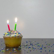 Ein bunter Cupcake mit zwei Geburtstagskerzen und bunten Streuseln.