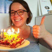 Frau Siemens-Gerth hält Kuchenstück mit Kerzen, lacht und zeigt den Daumen hoch.