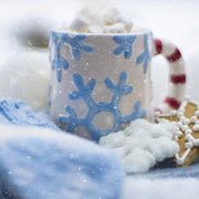 Blidausschnitt. Weißer Becher mit rot-weißem Griff und blauen Schneeflockenmuster. Auf dem Becher viele Mini-Marshmellows. Daneben Kekse in Stern- und Flockenform.. 